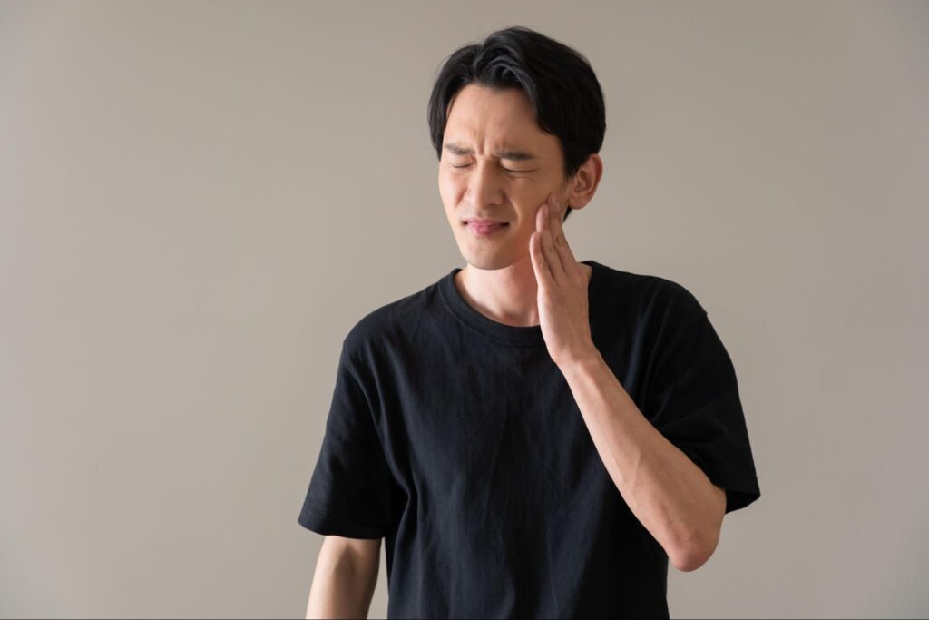 親知らずに痛みを感じて頬を押さえる男性