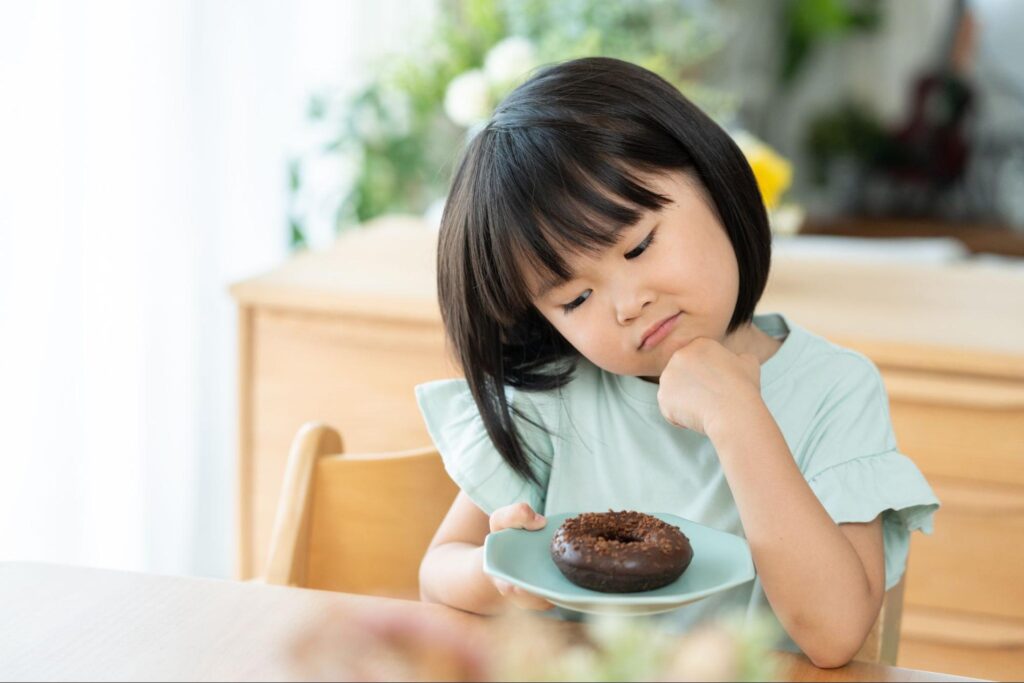 チョコレートドーナツの乗った皿を手に持って悩む子ども