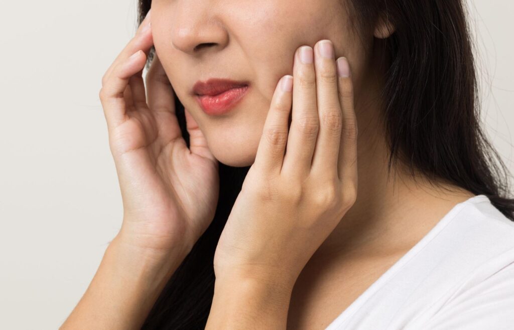 親知らずが生えかけで痛みがあり頬を押さえる女性
