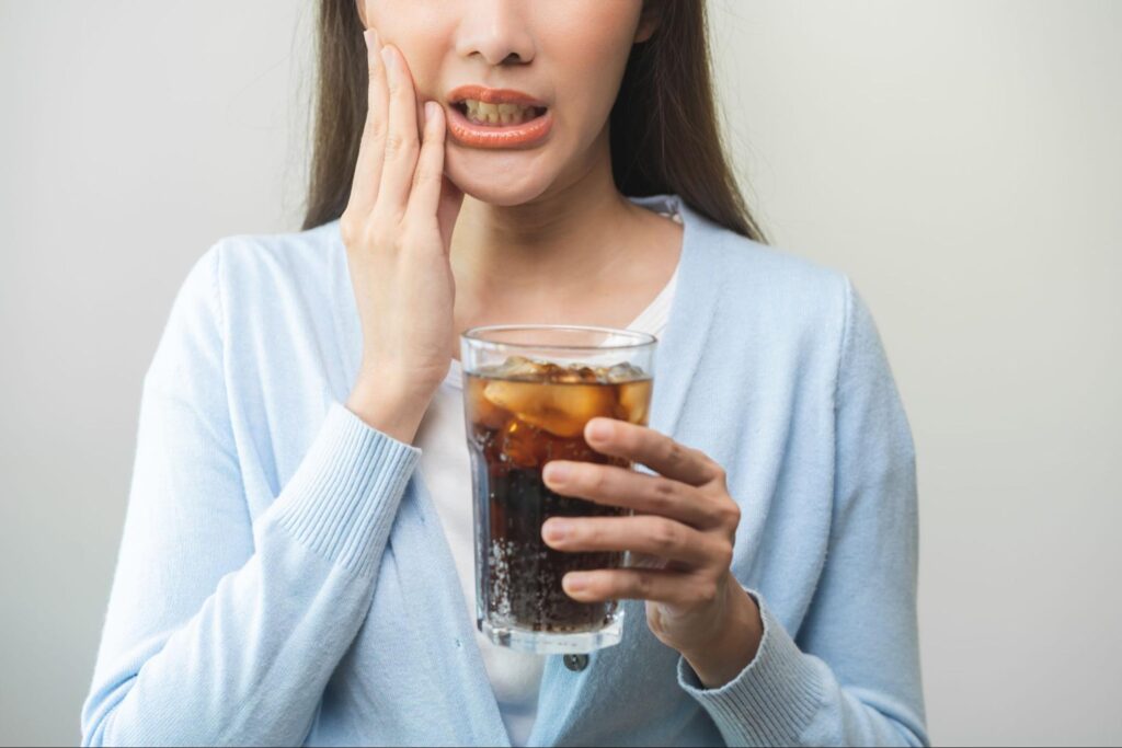 冷たい飲み物を飲んだら虫歯が痛み頬を押さえる女性