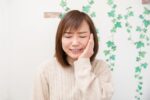 虫歯で歯が痛み頬を押さえる女性