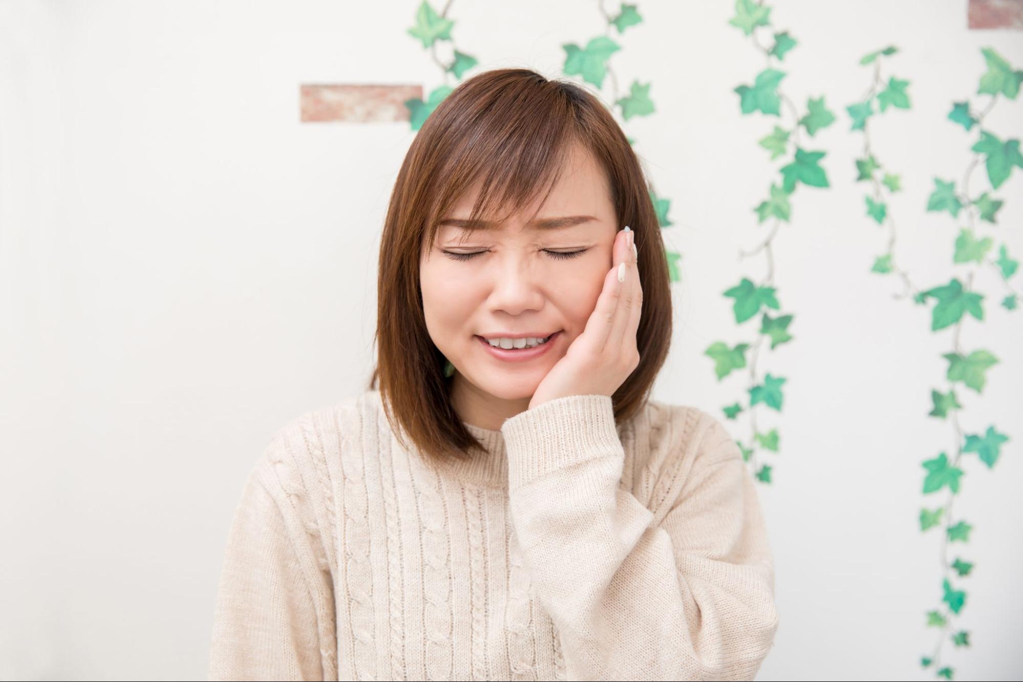 虫歯で歯が痛み頬を押さえる女性