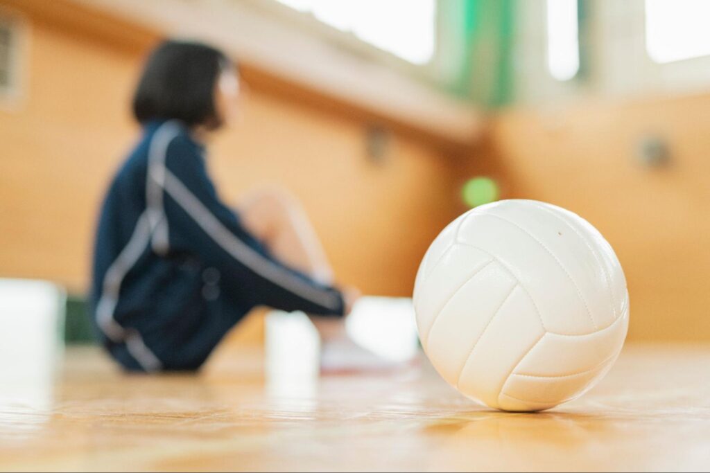 体育座りをしている若者とバレーボール　交通事故やスポーツ外傷での歯の損失のイメージ