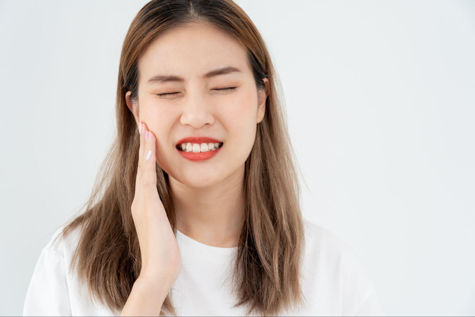 治療後の虫歯が痛くて頬を押さえる女性
