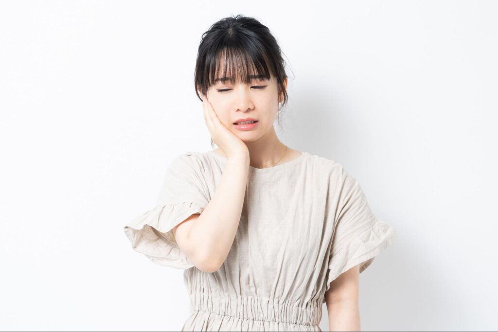 治療後の虫歯が痛くて頬を押さえる女性
