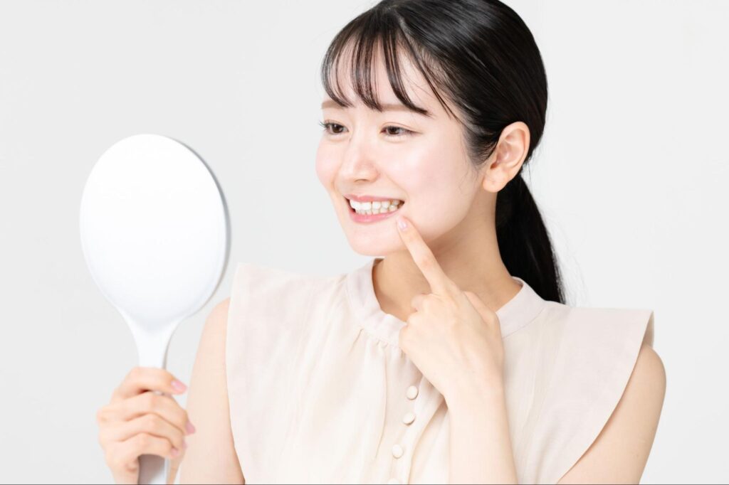 鏡を持ち笑顔で歯を見る女性