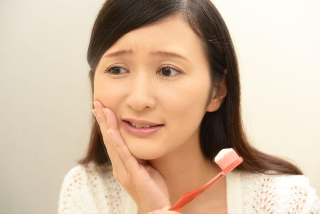 歯磨き中に虫歯が痛み頬を押さえる女性