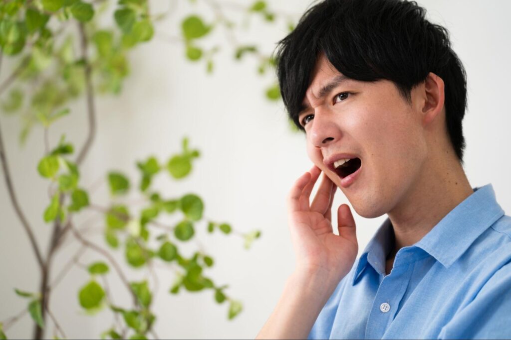虫歯で歯茎が腫れて痛みがあり頬を押さえる男性