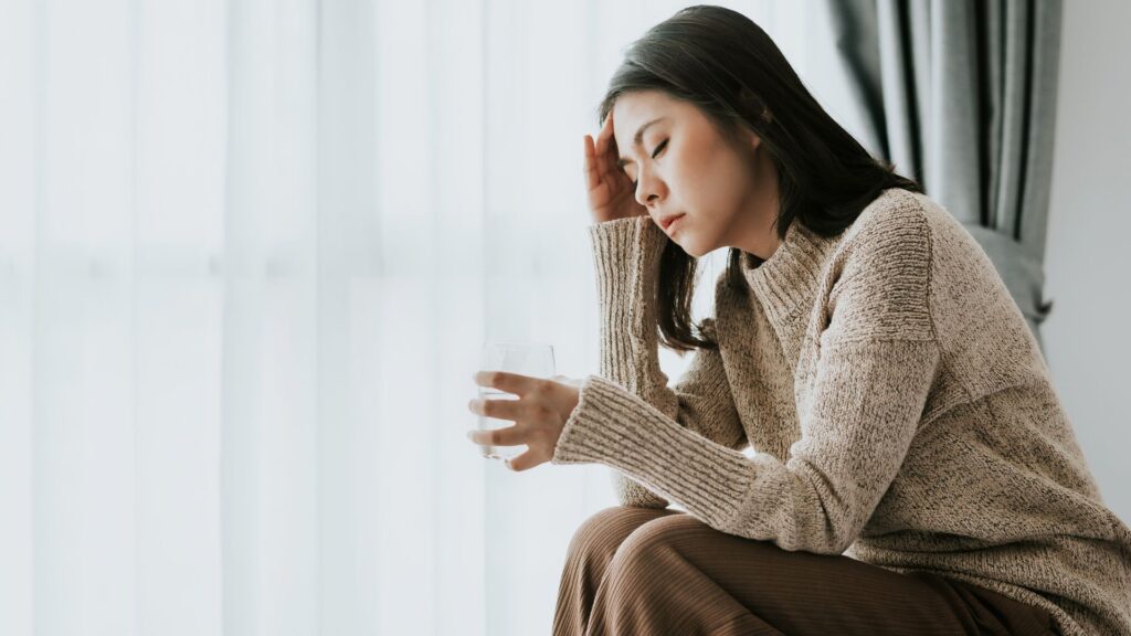 睡眠時無呼吸症候群による頭痛でつらそうにこめかみを押さえる女性
