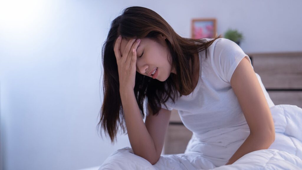 睡眠時無呼吸症候群の症状によって頭を抱えてつらそうにしている女性