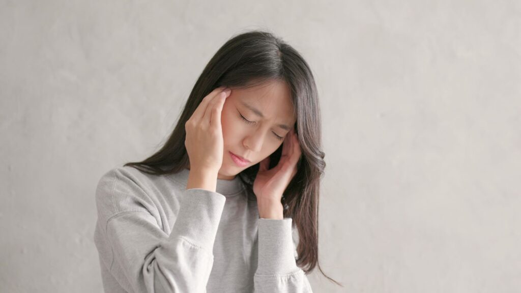 睡眠時無呼吸症候群による頭痛でつらそうにこめかみを押さえる女性